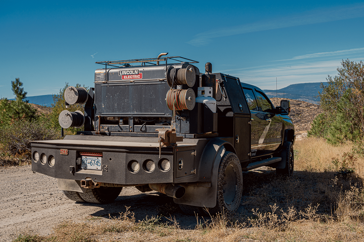 A truck with a large back end loaded with reels from Revel Industries driving on a dirt road