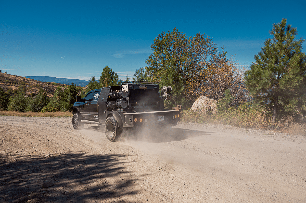 A truck towing a trailer navigates a dirt road, showcasing Revel Industries' reel service in action