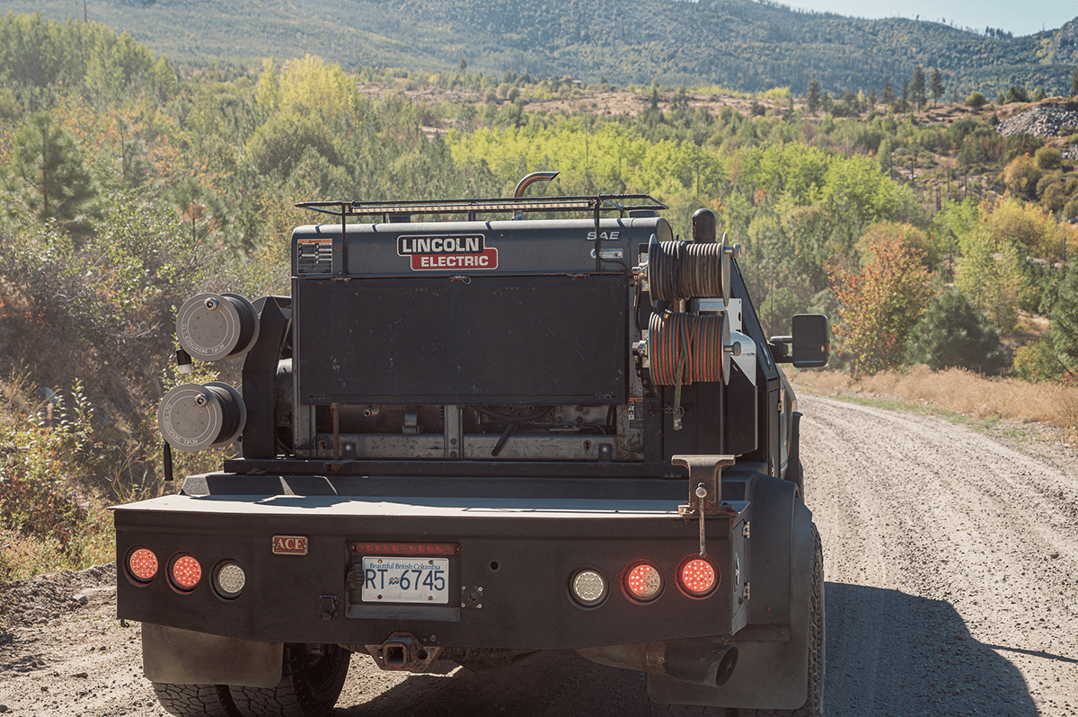 A truck navigates a dirt road, with a majestic mountain rising in the background under a clear blue sky