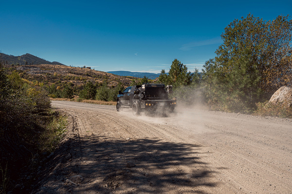 A service truck from Revel Industries drives down a dirt road, carrying reels with a hill in the background
