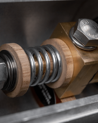 A close-up of a bronze reel featuring a metal spring and a wooden nut, showcasing intricate details and textures