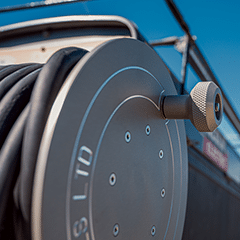 A close-up of a black hose coiled on a boat, showcasing its texture and the surrounding marine environment